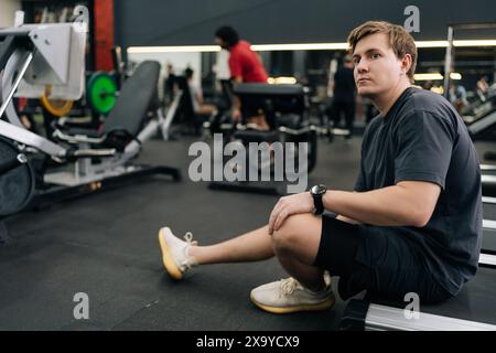 Gutaussehender, erschöpfter Läufer, der im Fitnessstudio eine Pause einlegt, sitzt auf dem Laufband. Porträt erschöpfter, schweißtreibender männlicher Atemnot nach Cardio-Training-Lauftraining Stockfoto