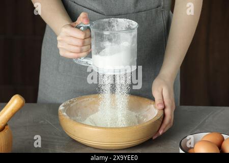 Frau siebt Mehl in eine Schüssel am grauen Tisch, Nahaufnahme Stockfoto