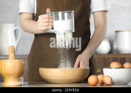 Frau siebt Mehl in eine Schüssel am Tisch in der Küche, Nahaufnahme Stockfoto