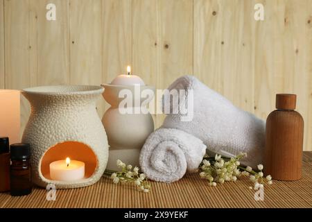 Aromatherapie. Duftende Kerzen, Flaschen, Blumen und Handtücher auf Bambusmatte Stockfoto