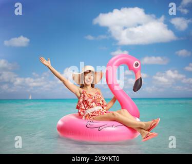 Junge glückliche Frau, die auf einem Flamingo-Gummiring im Meer sitzt Stockfoto