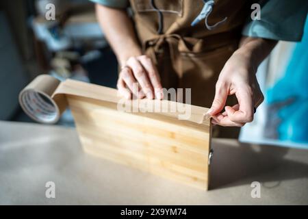 Handflächen von vorsichtigen Künstlerinnen, die Kanten von hölzernen Leinwandplatten für die weitere Arbeit mit Epoxidharz verkleben Stockfoto