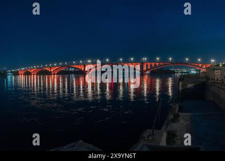 Eine Brücke, die in der Nacht über ein Gewässer überquert, vor einer Stadtlandschaft mit Himmel und Horizont im Hintergrund Stockfoto