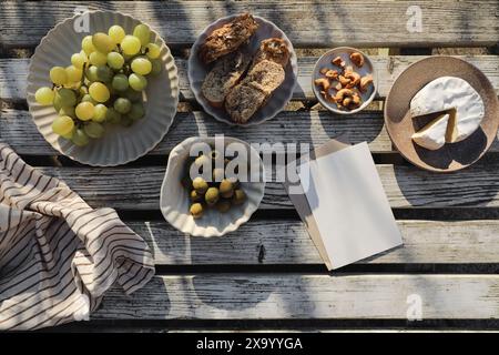 Sommeressen, Picknick. Brie-Käse, Traubenfrüchte, Oliven und Cashewnüsse. Brot, Baguette. Vintage, weißer Holztisch mit Blick auf die Tischplatte. Grußkarte Stockfoto