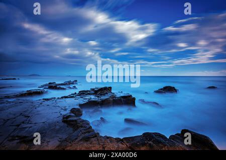 Felsiger Strand, der während der blauen Stunde bei Vollmondlicht beleuchtet wird: Dämmerung in Mooloolaba, Queensland, Australien Stockfoto