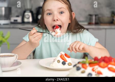 Das fröhliche kleine Mädchen isst Kuchen und steckt ihr ein großes Stück Dessert in den Mund. Ausgewählter Fokus. Hochwertige Fotos Stockfoto