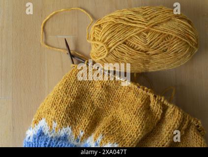 Flachbild-Fotografie eines aus isländischer Wolle gestrickten Lopeysa-Pullovers mit gelber Garnkugel auf runden Nadeln auf Holzuntergrund Stockfoto