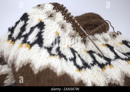 Nahaufnahme eines braunen, weißen, schwarzen isländischen Wollstrickpullovers mit Pinguin-Muster auf den Nadeln Stockfoto