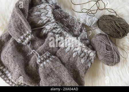 Flachbild-Fotografie eines beigen isländischen Wollgestrickten Lopeysa-Pullovers auf den Nadeln mit Garnbällchen Stockfoto