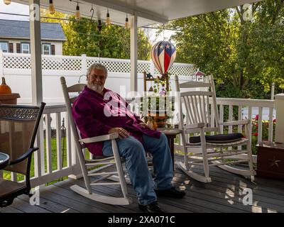 Ein älterer Mann, der sich auf einem Schaukelstuhl auf einer Veranda entspannt Stockfoto