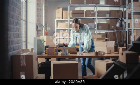 Warehouse weibliche Vertriebsleiterin mit Laptop-Computer, die ein kleines Paket für den Versand vorbereitet. Wunderschöner Inhaber kleiner Unternehmen, der im Online-Store arbeitet und die Bestellung für den Kunden vorbereitet. Stockfoto