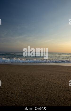 Sonnenuntergang über Sandstrand mit Wellen am Ufer Stockfoto