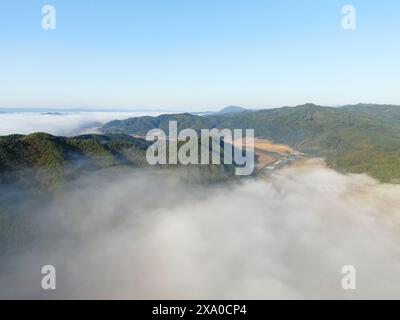 Nebelige Berge im Tal mit Fluss und Feldern darunter Stockfoto