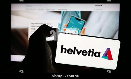 Person mit Smartphone mit Logo der Schweizer Versicherungsgesellschaft Helvetia Holding AG vor der Website. Schwerpunkt auf dem Display des Telefons. Stockfoto