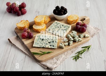 Bio-Blauschimmelkäse mit Trauben und Oliven auf einem Holzbrett, Seitenansicht. Stockfoto