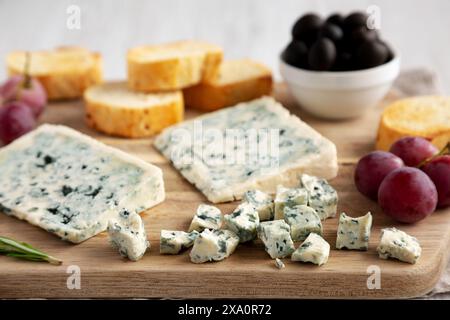 Bio-Blauschimmelkäse mit Trauben und Oliven auf einem Holzbrett, Seitenansicht. Stockfoto