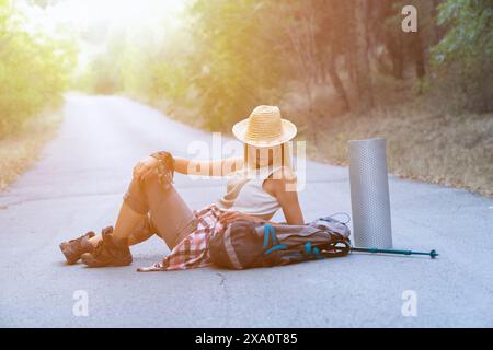 Eine Reisende Frau sitzt auf der Straße mit ihrem Rucksack neben ihr. Reise- und Reisekonzept Stockfoto