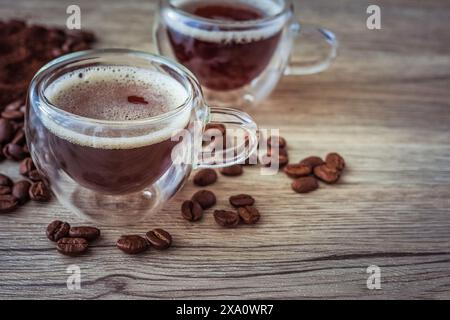 Glasbecher mit amerikanischem Kaffee, umgeben von Kaffeebohnen und gemahlenem Kaffee auf Holzbrett Stockfoto