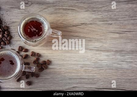 Glasbecher mit amerikanischem Kaffee, umgeben von Kaffeebohnen und gemahlenem Kaffee auf Holzbrett Stockfoto