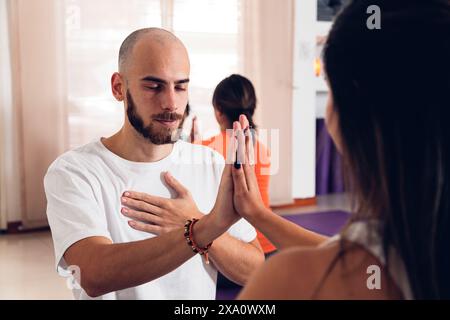 Junge Paare, die Hände berühren, während sie gemeinsam im Studio Yoga-Haltung üben. Stockfoto