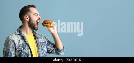 Hungriger Mann isst leckeren Burger auf hellblauem Hintergrund mit Platz für Text Stockfoto