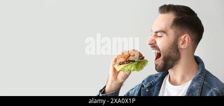 Hungriger Mann isst leckeren Burger auf hellem Hintergrund mit Platz für Text Stockfoto