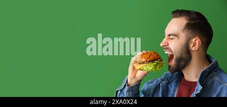 Hungriger Mann isst leckeren Burger auf grünem Hintergrund mit Platz für Text Stockfoto