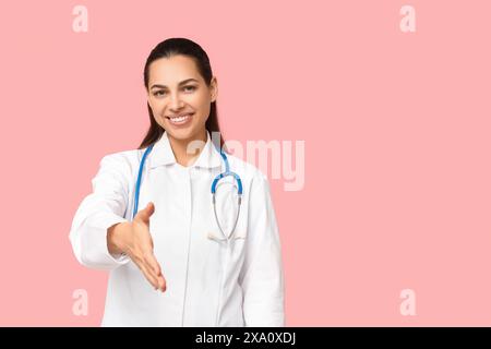 Porträt einer Ärztin, die nach einem Handschlag auf rosa Hintergrund streckt Stockfoto