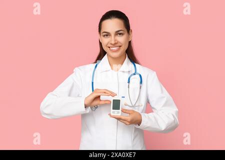 Porträt einer Ärztin mit tragbarem Blutzuckermessgerät auf rosa Hintergrund Stockfoto