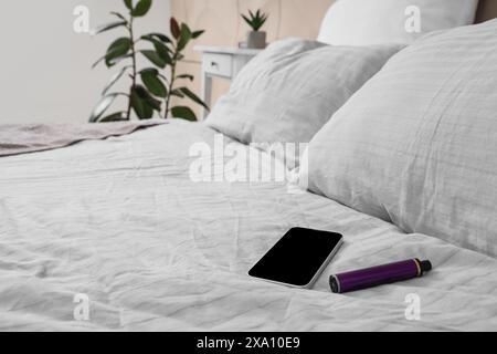 Lila elektronische Einweg-Zigarette und Mobiltelefon auf dem Bett im Zimmer Stockfoto