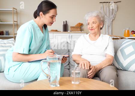 Physiotherapeutin schreibt in Zwischenablage mit Seniorin zu Hause Stockfoto