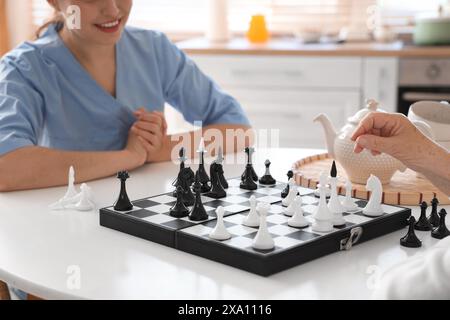 Physiotherapeutin mit einer älteren Frau, die Schach am Tisch in der Küche spielt, Nahaufnahme Stockfoto