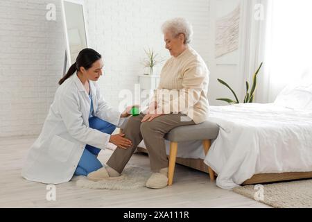 Physiotherapeutin mit Ballmassage des Oberschenkels der Seniorin im Schlafzimmer Stockfoto