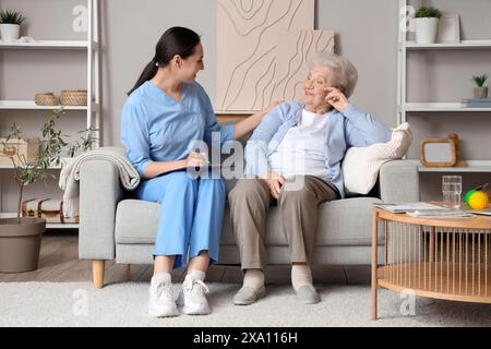 Ältere Frau mit Physiotherapeutin, die zu Hause auf dem Sofa in die Zwischenablage schreibt Stockfoto