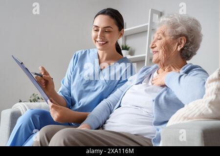 Physiotherapeutin mit Klemmbrett und ältere Frau, die zu Hause auf dem Sofa sitzt Stockfoto