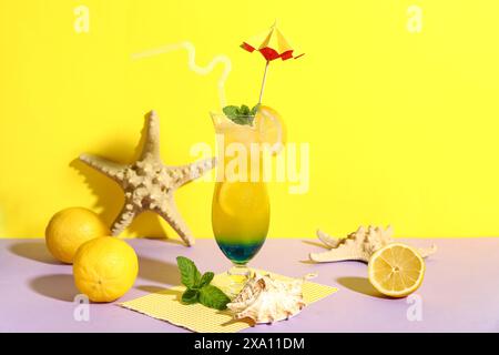 Ein Glas leckerer Cocktail mit Zitrone, Muscheln und Seesternen auf farbenfrohem Hintergrund Stockfoto