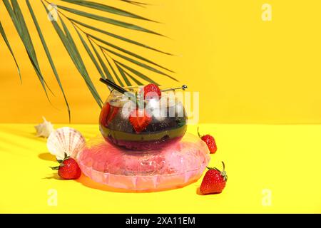 Glas leckerer Cocktail mit Erdbeere, Muscheln, Palmblatt und aufblasbarem Ring auf farbenfrohem Hintergrund Stockfoto