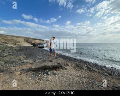 Ein Mann mit einem großen Rucksack steht an der felsigen Küste am Meer, Teneriffa in Spanien Stockfoto