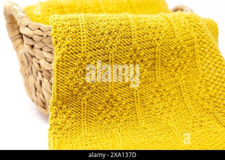 Nahaufnahme einer gelben Strickdecke im Diamantstrickmuster in einem Korb auf weißem Hintergrund Stockfoto