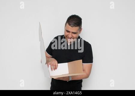 Dunkelhäutiger erwachsener Latino-Mann baut einen Karton, der den Anweisungen folgt, konzentriert und aufmerksam zusammen Stockfoto