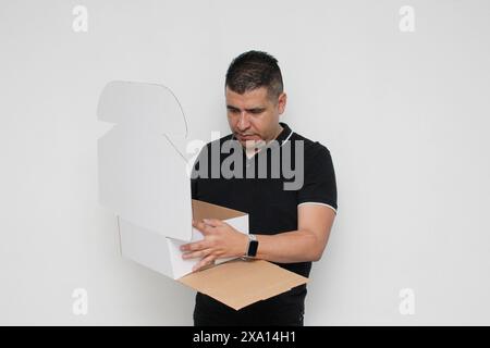 Dunkelhäutiger erwachsener Latino-Mann baut einen Karton, der den Anweisungen folgt, konzentriert und aufmerksam zusammen Stockfoto