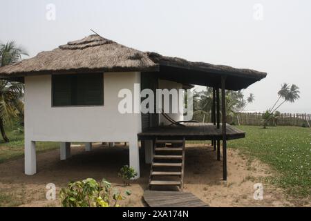 Ein modernes Haus auf Stelzen mit einem Strohdach, in einem grasbewachsenen Bereich in der Nähe des Strandes gelegen. Stockfoto