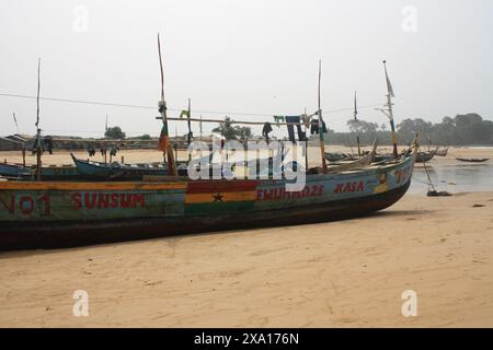 Am Sandstrand eines ghanaischen Küstendorfes liegt ein großes, hell bemaltes Fischerboot. Die lebendigen Farben und detailgetreuen Grafiken auf der Bootsreferenz Stockfoto