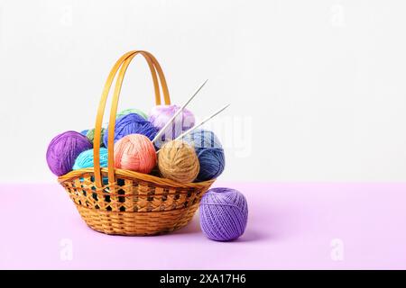 Viele bunte Strickbälle in einem Korb mit Stricknadeln auf einem pastellfarbenen lila Hintergrund. Set für das Hobbys, warme Kleidung oder Spielzeug zu stricken. Konzeptnadelarbeit Stockfoto