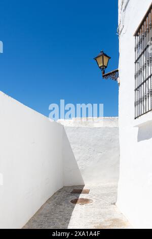 Eine weiße Ziegelwand mit schwarzen Metallstangen und einer hängenden Straßenleuchte in Vejer de la Frontera, Spanien Stockfoto