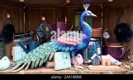 Gartenschmuck zum Verkauf, ein farbenfroher Pfau und andere Ornamente auf einem Holzregal. Stockfoto