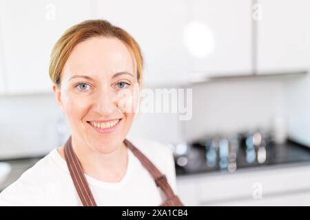 Eine Frau mit blonden Haaren und blauen Augen lächelt vor einer Küchenzeile Stockfoto