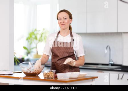Eine Frau steht in einer Küche, trägt eine Schürze und bereitet Essen zu Stockfoto