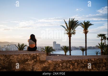 Junge Frau, die den Sonnenuntergang von den Stadtmauern des Schlosses Papa Luna in Peñiscola, Castellon, Valencianische Gemeinde, Spanien genießt Stockfoto