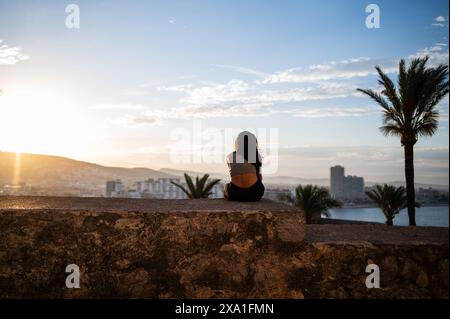 Junge Frau, die den Sonnenuntergang von den Stadtmauern des Schlosses Papa Luna in Peñiscola, Castellon, Valencianische Gemeinde, Spanien genießt Stockfoto